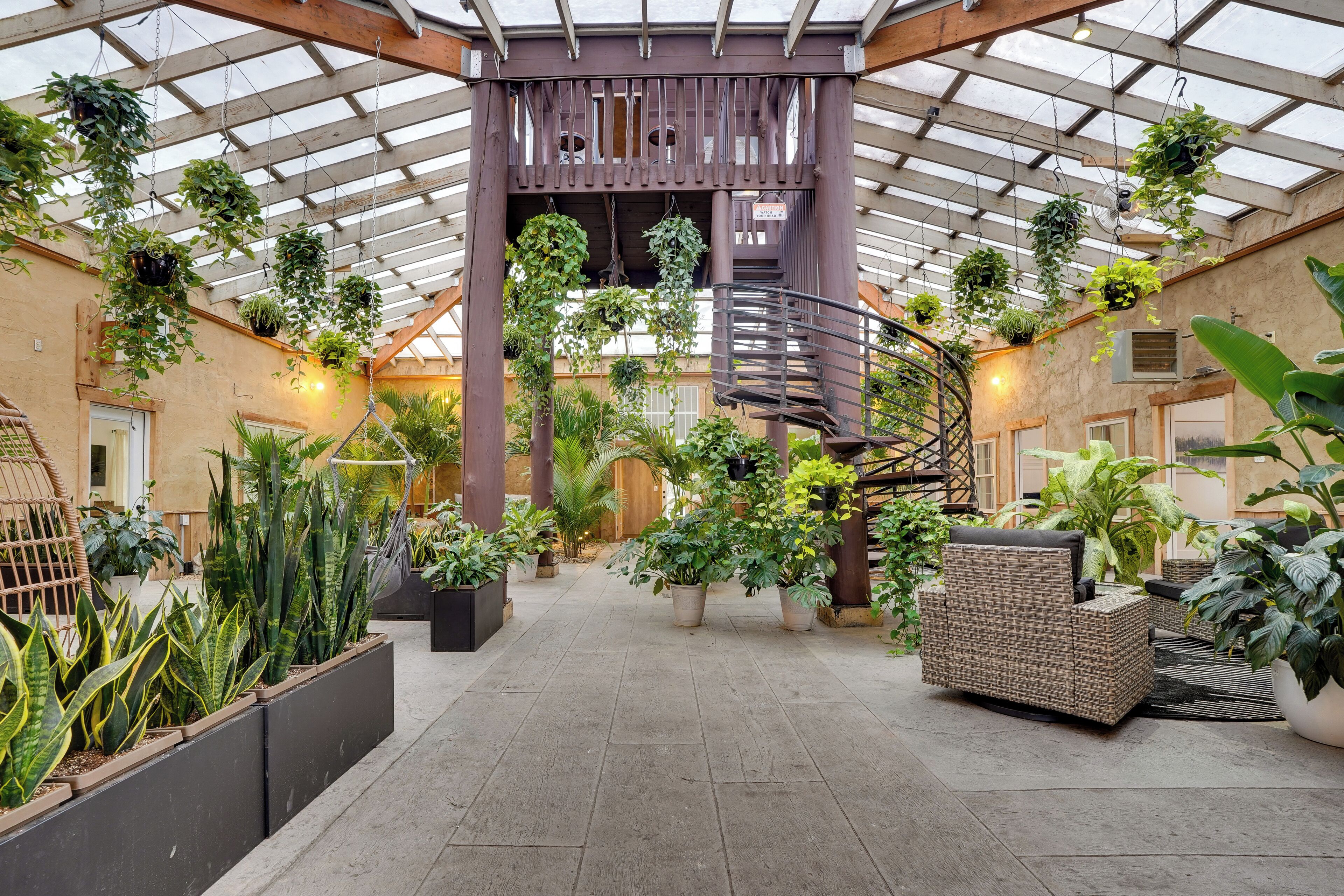 A spacious atrium with a central spiral staircase, surrounded by various potted plants and wicker furniture.