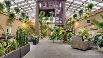 A spacious atrium with a central spiral staircase, surrounded by various potted plants and wicker furniture.
