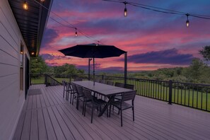 A deck with a table and chairs, an umbrella, and string lights against a sunset sky.