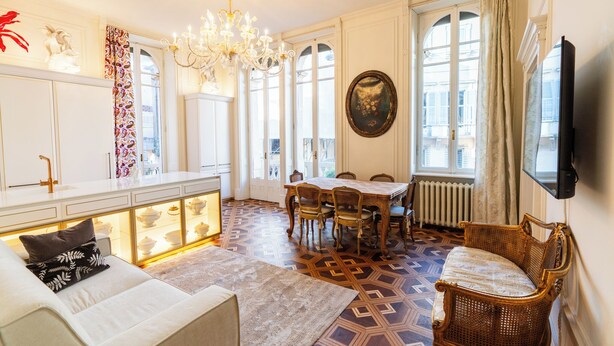A dining area with a chandelier, a table with chairs, and a sofa. - Appartamento Catullo Imperiale (Verona)