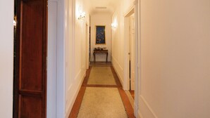 A narrow hallway with a wooden door on the left, a small table with a painting in the center, and a white door on the right. - Appartamento Catullo Imperiale (Verona)