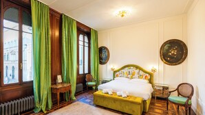 A room with a large bed, green curtains, a wooden floor, and a view of buildings outside. - Appartamento Catullo Imperiale (Verona)