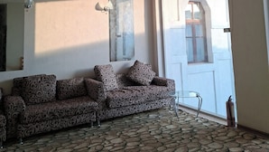 Una habitación con un sofá estampado, una alfombra con diseño, un techo con motivos geométricos y una puerta con señal de salida.
