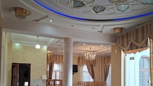 Amplia habitación con techo alto, diseño ornamental en el techo, candelabros y un gran ventanal con cortinas.