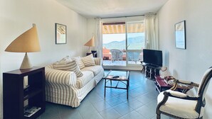 A living room with a sofa, a coffee table, a TV, and a balcony with a view. - Pool & Seaview apartment (La Croix-Valmer)