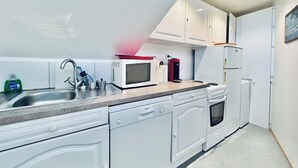 A modern kitchen with white cabinets, a stainless steel sink, a Bosch dishwasher, a red coffee maker, and a white refrigerator. - Pool & Seaview apartment (La Croix-Valmer)