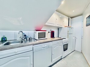 A modern kitchen with white cabinets, a stainless steel sink, a Bosch dishwasher, a red coffee maker, and a white refrigerator. - Pool & Seaview apartment (La Croix-Valmer)