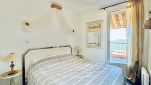 A bedroom with a bed, bedside lamps, a mirror, and a view of a balcony. - Pool & Seaview apartment (La Croix-Valmer)