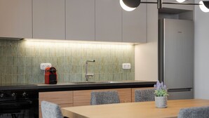 Cocina moderna con refrigerador de acero inoxidable, horno empotrado y lavamanos con grifo. Dos lámparas de pared sobre la encimera.