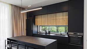 A modern kitchen with a central island, dark cabinetry, and a window providing a view of greenery. - Ioannina Secret Luxury Villas (Vounoplagia)