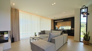 A modern living room with a grey sectional sofa, a small round coffee table, and a flat-screen TV. - Ioannina Secret Luxury Villas (Vounoplagia)