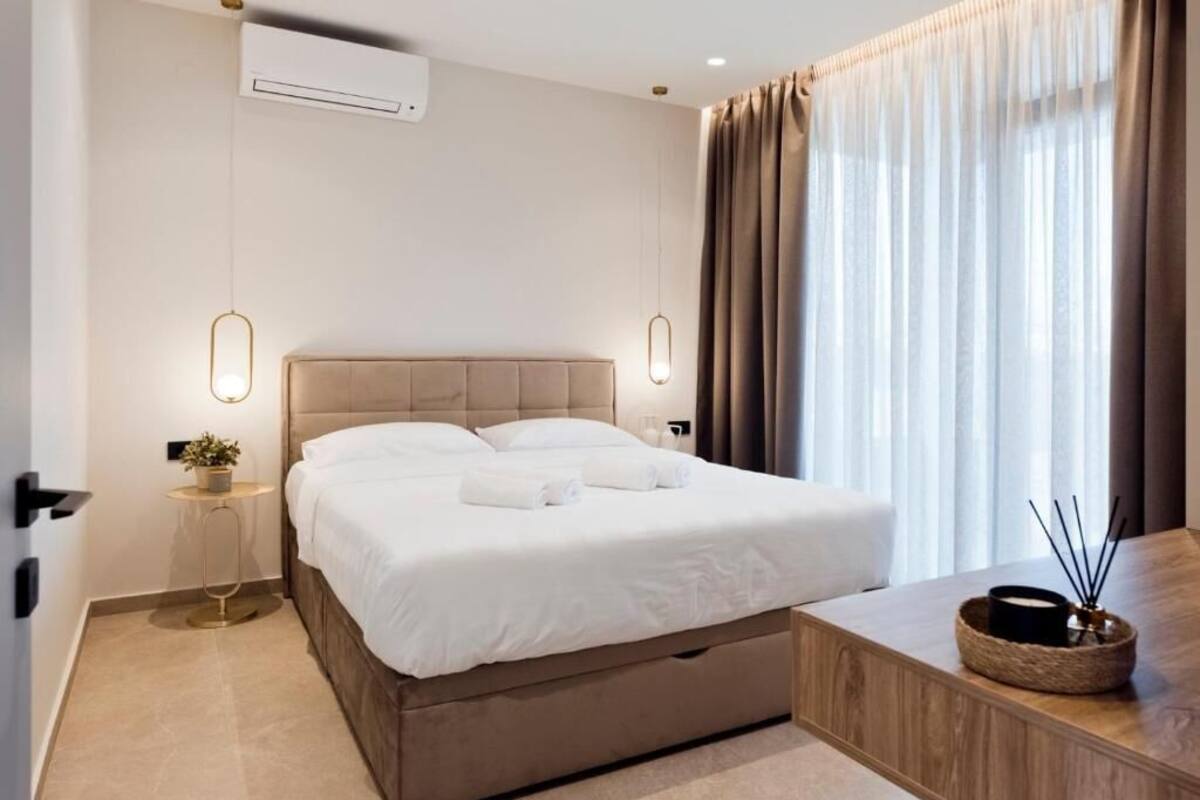 A modern hotel room with a large bed, bedside tables, a small side table, a bedside lamp, and a window with curtains.