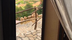 Vista desde un balcón con suelo de piedra, que da a un paisaje costero con vegetación y edificios.