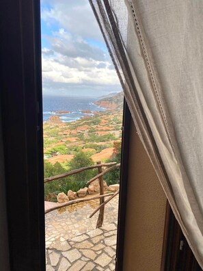 Blick von einem Balkon mit Steinboden auf eine Küstenlandschaft mit Grünflächen und Gebäuden.