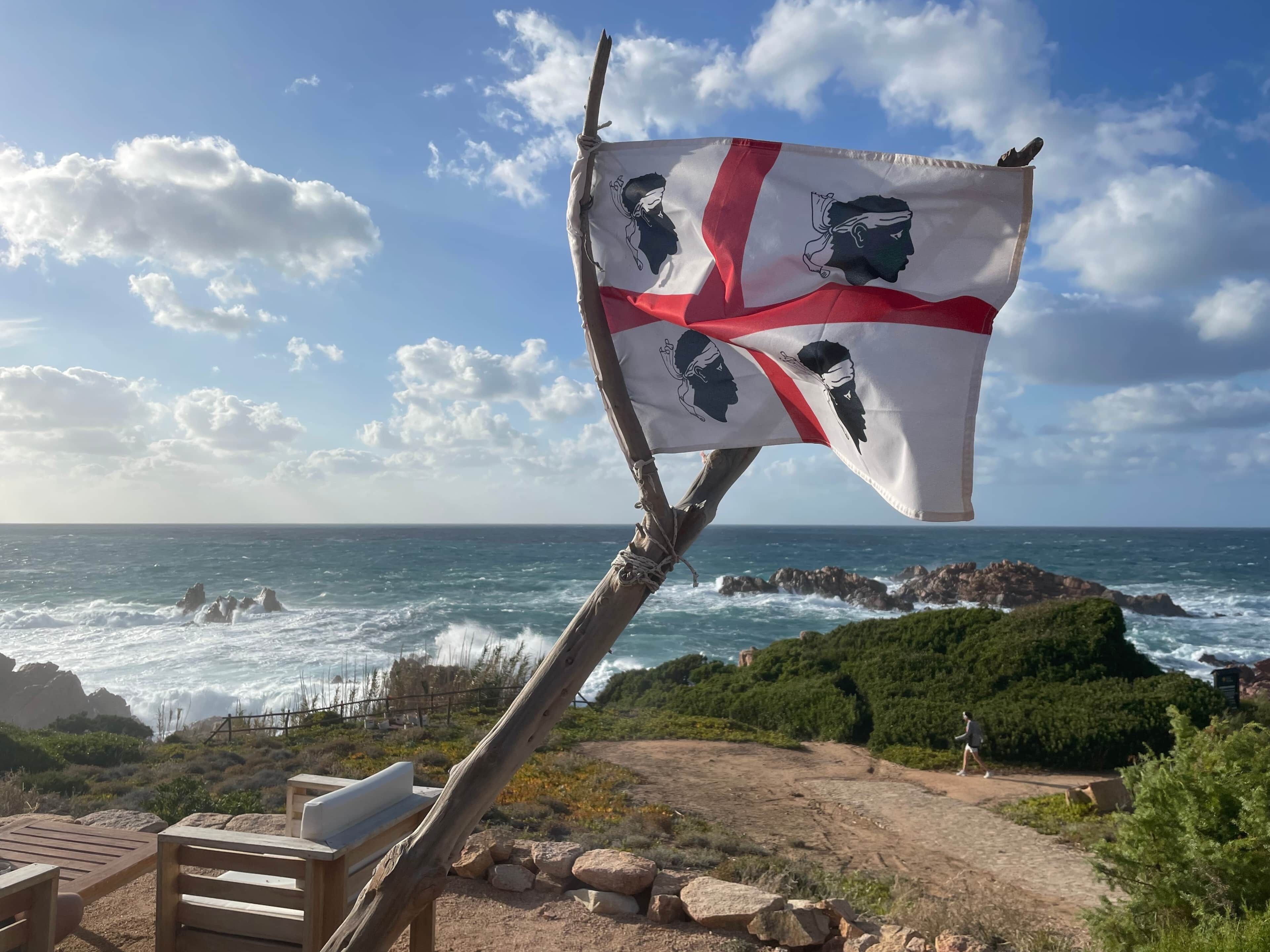 Una bandera en un asta con vista al mar y terreno rocoso.