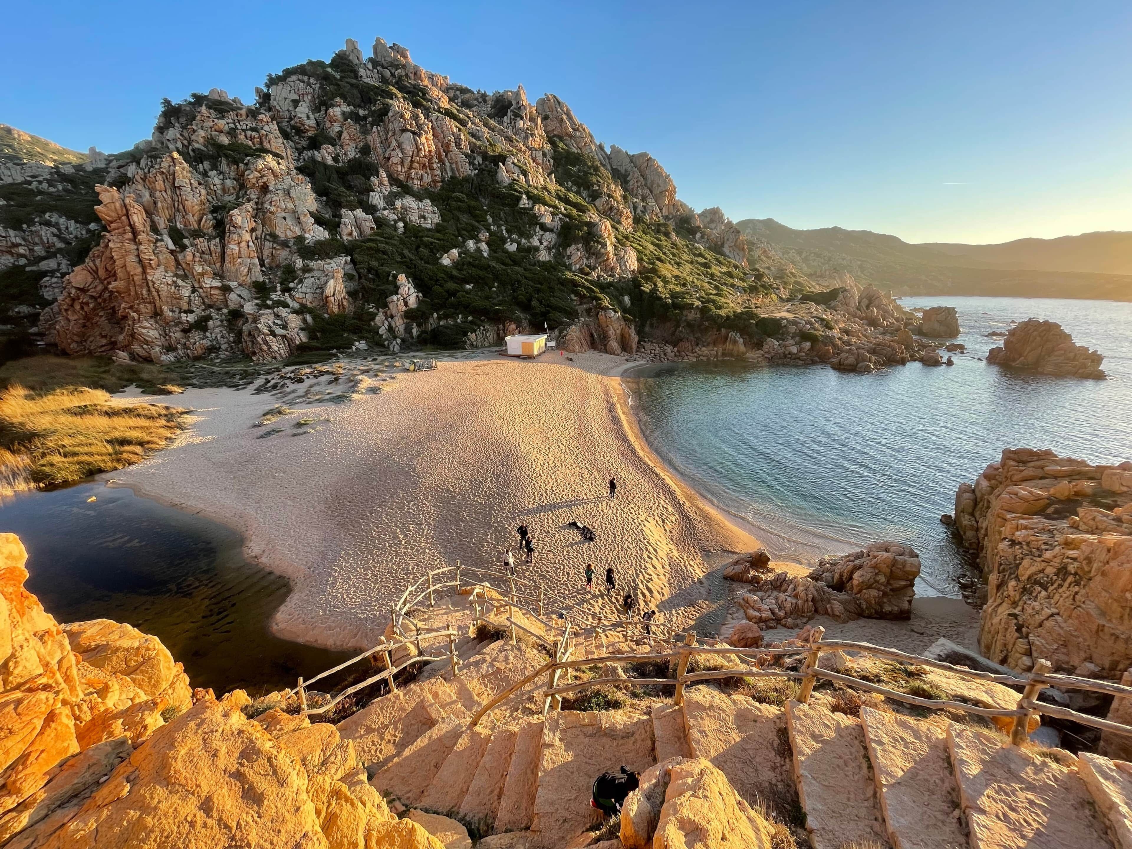 Un paisaje costero con un acantilado rocoso, una playa arenosa y una pequeña construcción.