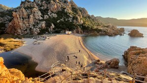 Un paisaje costero con un acantilado rocoso, una playa arenosa y una pequeña construcción.