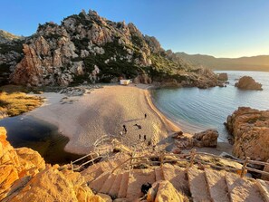 Eine Küstenlandschaft mit einem felsigen Klippen, einem Sandstrand und einem kleinen Gebäude.