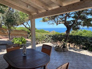 A wooden pergola with a table and chairs, overlooking a coastal landscape with trees and a view of the sea. - Ginepri Villa - sea view (Costa Paradiso)