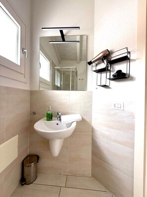 Un baño moderno con un lavamanos pedestal, un espejo, un perchero y un cubo de basura.