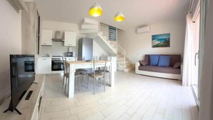 Un appartamento moderno con zona pranzo, cucina, scala, divano e TV.
