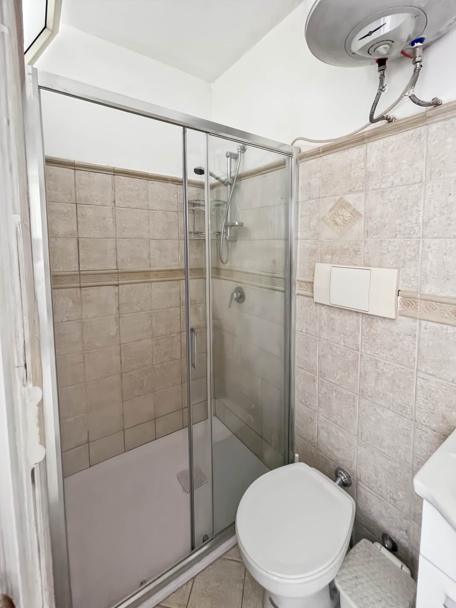 Ein Badezimmer mit Duschkabine aus Glas, Toilette und Wandwaschbecken.