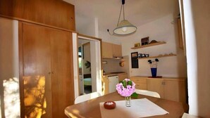 Cocina compacta con muebles de madera, una mesa de comedor con un florero y una lámpara colgante.