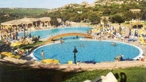 Una gran piscina al aire libre rodeada de sillas de descanso y sombrillas, con montañas al fondo.