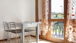 Un coin repas avec une table et des chaises, une porte en bois avec des rideaux et une vue sur le mobilier d’extérieur.