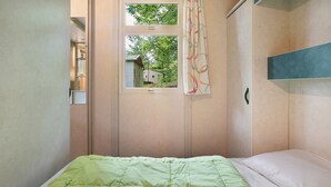 A small bedroom with a single bed, a window with a view of a house, and a curtain.