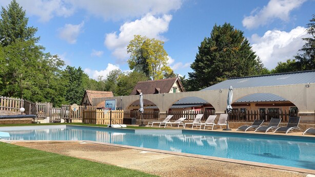 A swimming pool with lounge chairs, a wooden fence, and a building with a sloped roof.