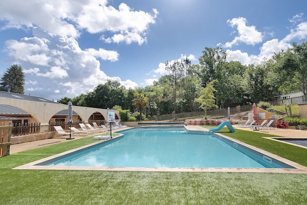 A swimming pool with a slide, surrounded by a wooden fence, and a grassy area with lounge chairs.