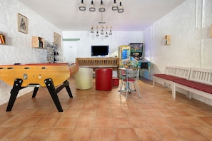 A room with a foosball table, a bench, a red cylindrical object, and a television.