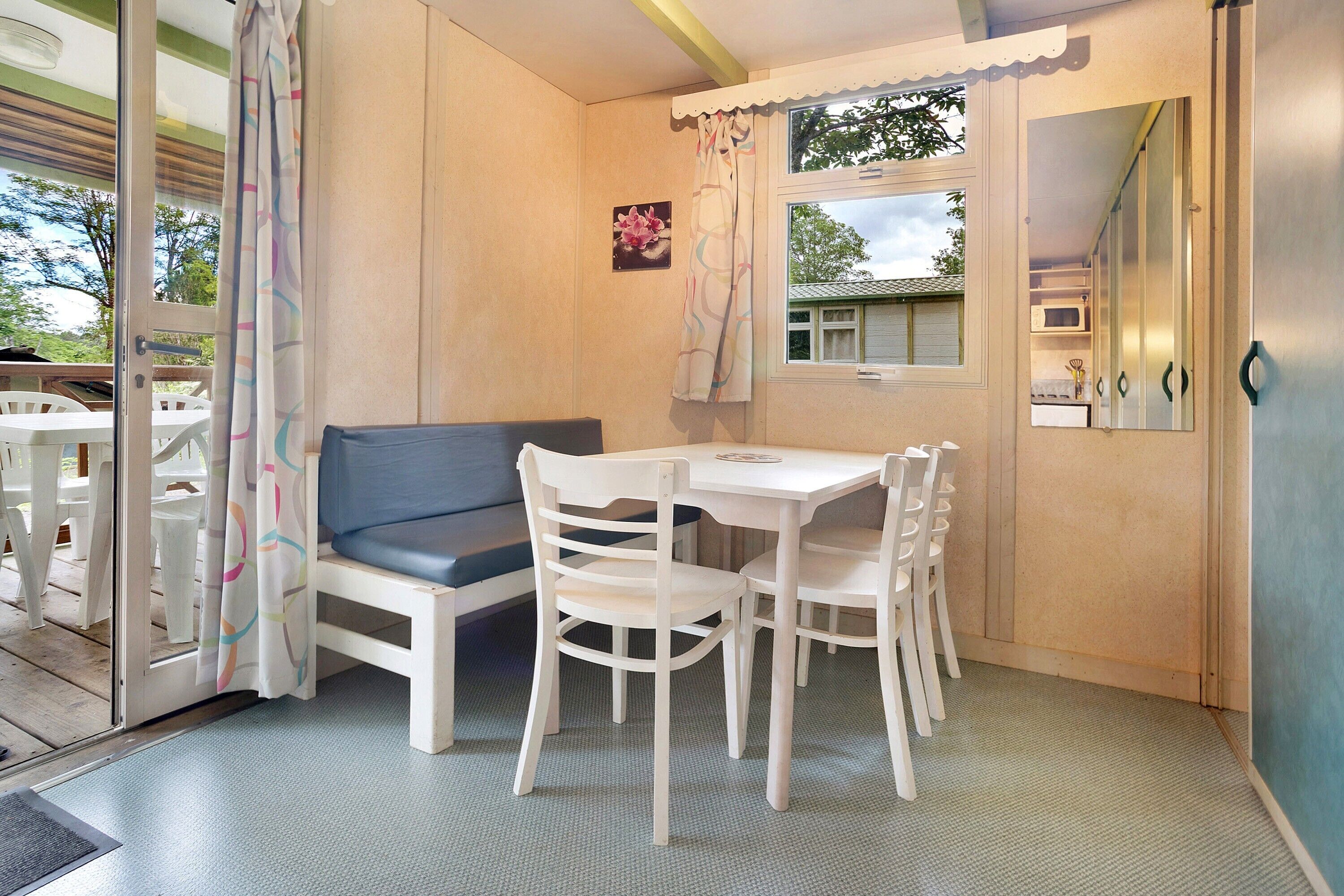 A room with a table and chairs, a sofa, a window with curtains, and a door leading to another room.