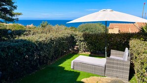 Un jardín con un sofá de mimbre y una sombrilla blanca, con vistas a la costa.