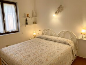 A neatly made bed with a floral-patterned bedspread, a white metal headboard, and bedside lamps. - Villetta La Risacca (Costa Paradiso)
