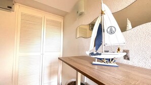 Una habitación con una mesa de madera, una maqueta de velero, un armario blanco con persianas horizontales, un aire acondicionado montado en la pared y una pared con textura.
