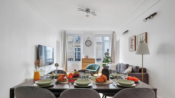 Un coin repas avec une table dressée pour quatre personnes, un canapé, une lampe et une horloge au mur.