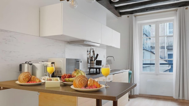 Eine moderne Küche mit Marmorfliesenspiegel, einer Kaffeemaschine, einem Toaster und einer Obstschale mit Croissants und Trauben.