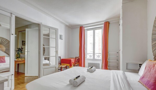Quarto de hotel com uma cama grande, uma mesa, uma cadeira e uma janela com cortinas.