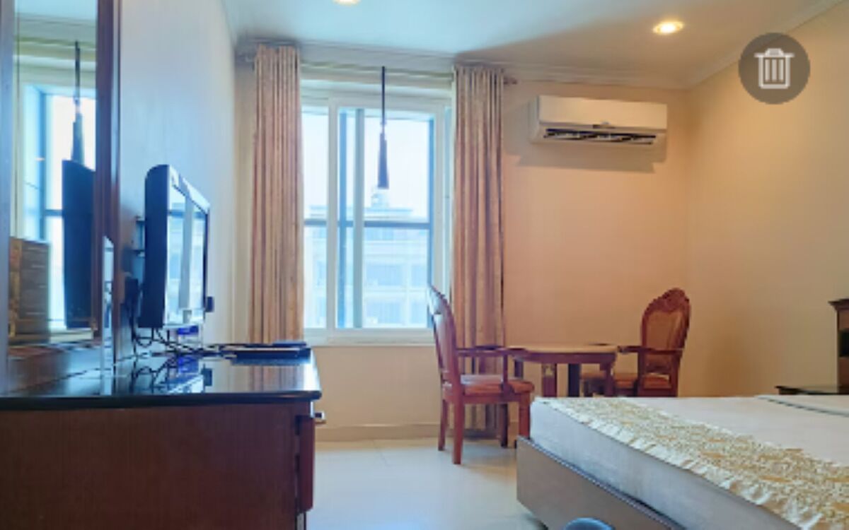 A hotel room with a bed, a desk with a computer, a chair, and a window with curtains.