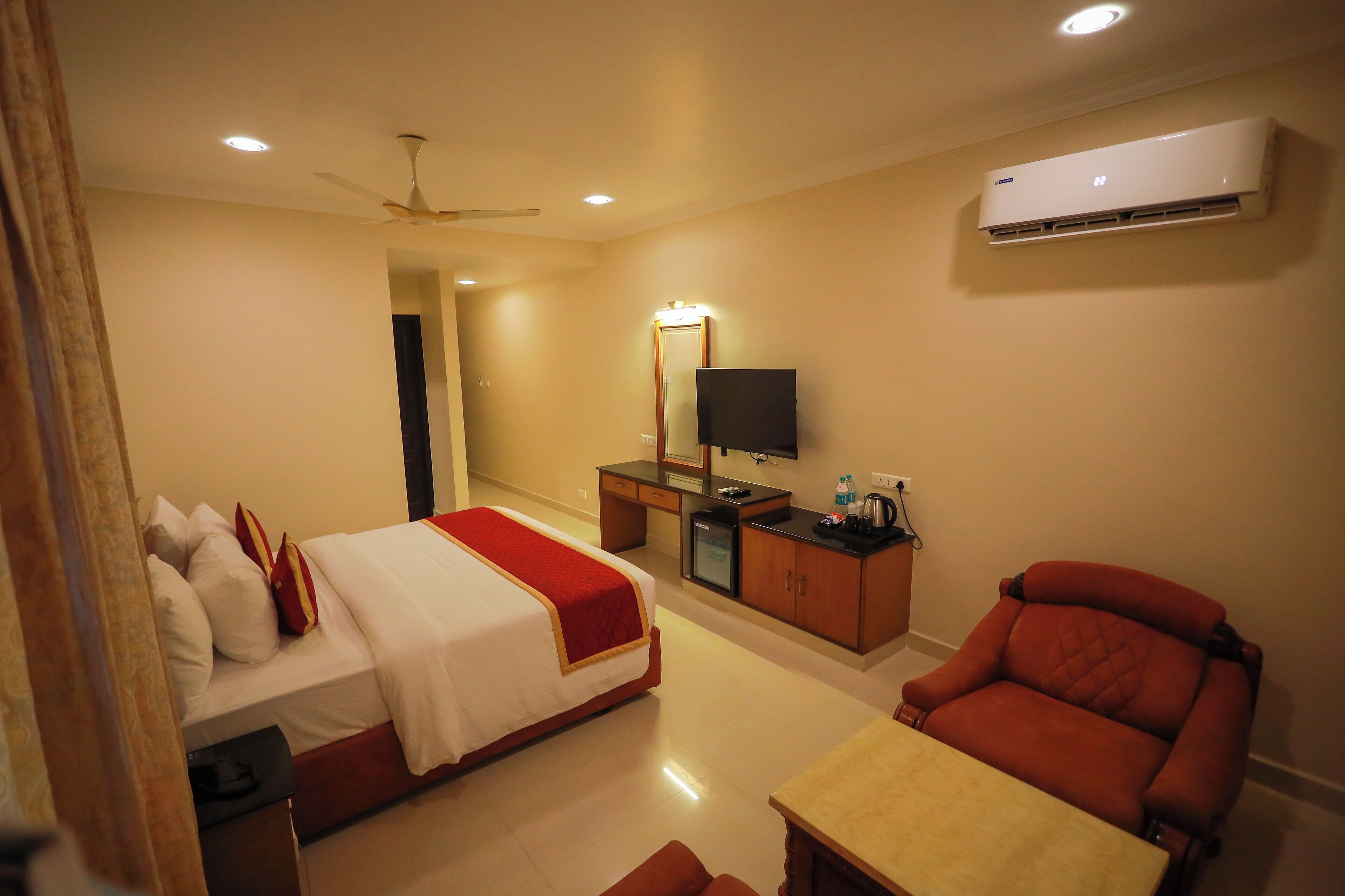 A hotel room with a bed, a desk, a chair, a television, and an air conditioning unit.