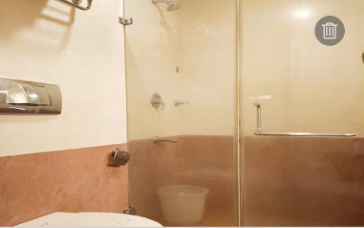 A bathroom with a glass shower enclosure, a toilet, and a trash bin.