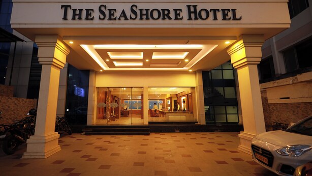 The exterior of The Seashore Hotel with a well-lit entrance, a tiled pavement, and a parked car.