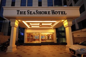Exterior del Hotel Seashore con una entrada bien iluminada, un pavimento adoquinado y un coche estacionado.