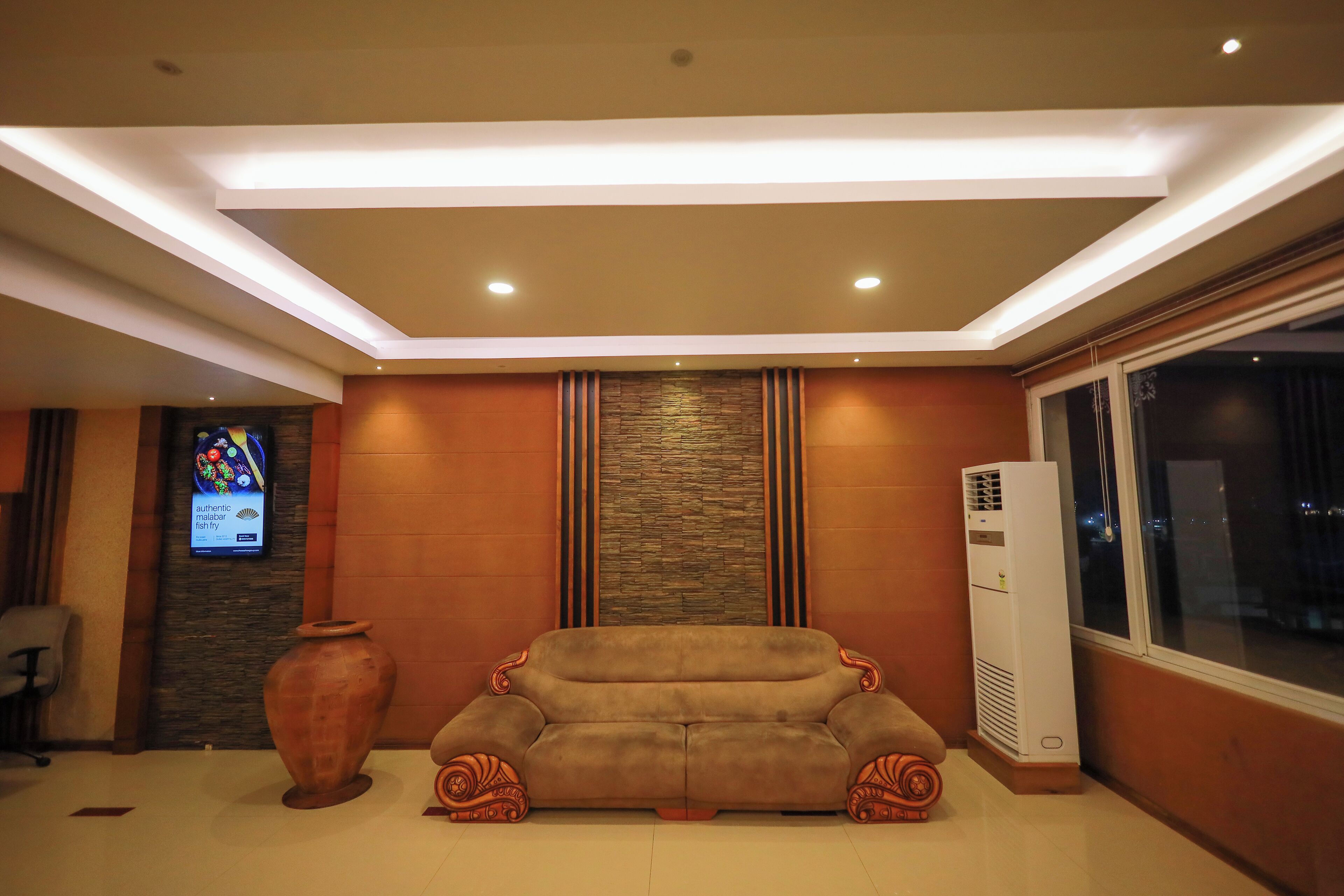 A modern living room with a sofa, a large vase, and a wall-mounted TV.