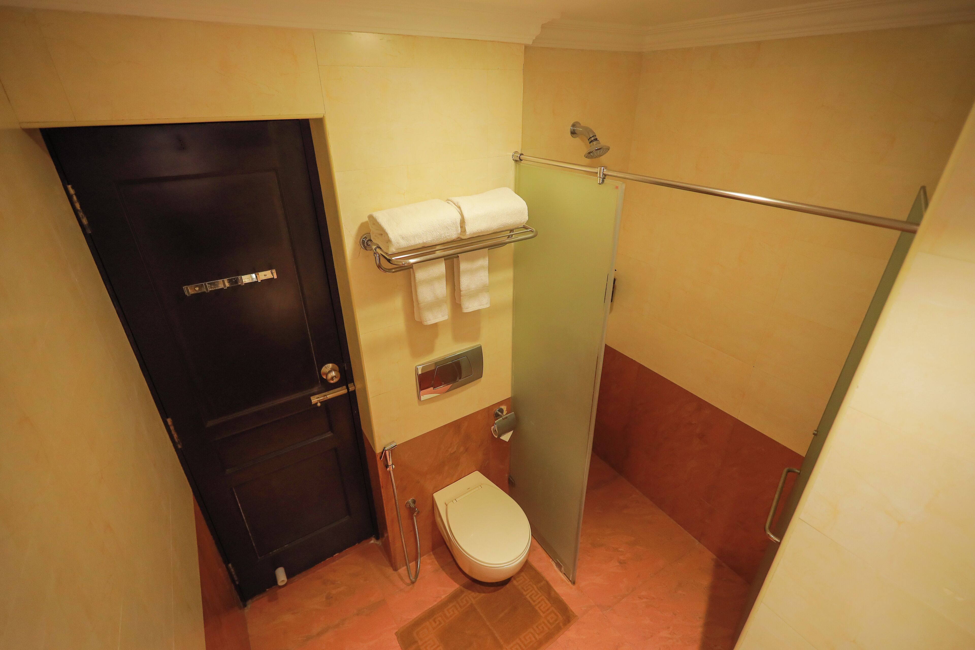 A compact bathroom with a toilet, a towel rack, and a shower area.
