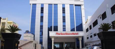 The Sea Shore Hotel with a modern facade, a covered entrance, and a parking area with several cars.