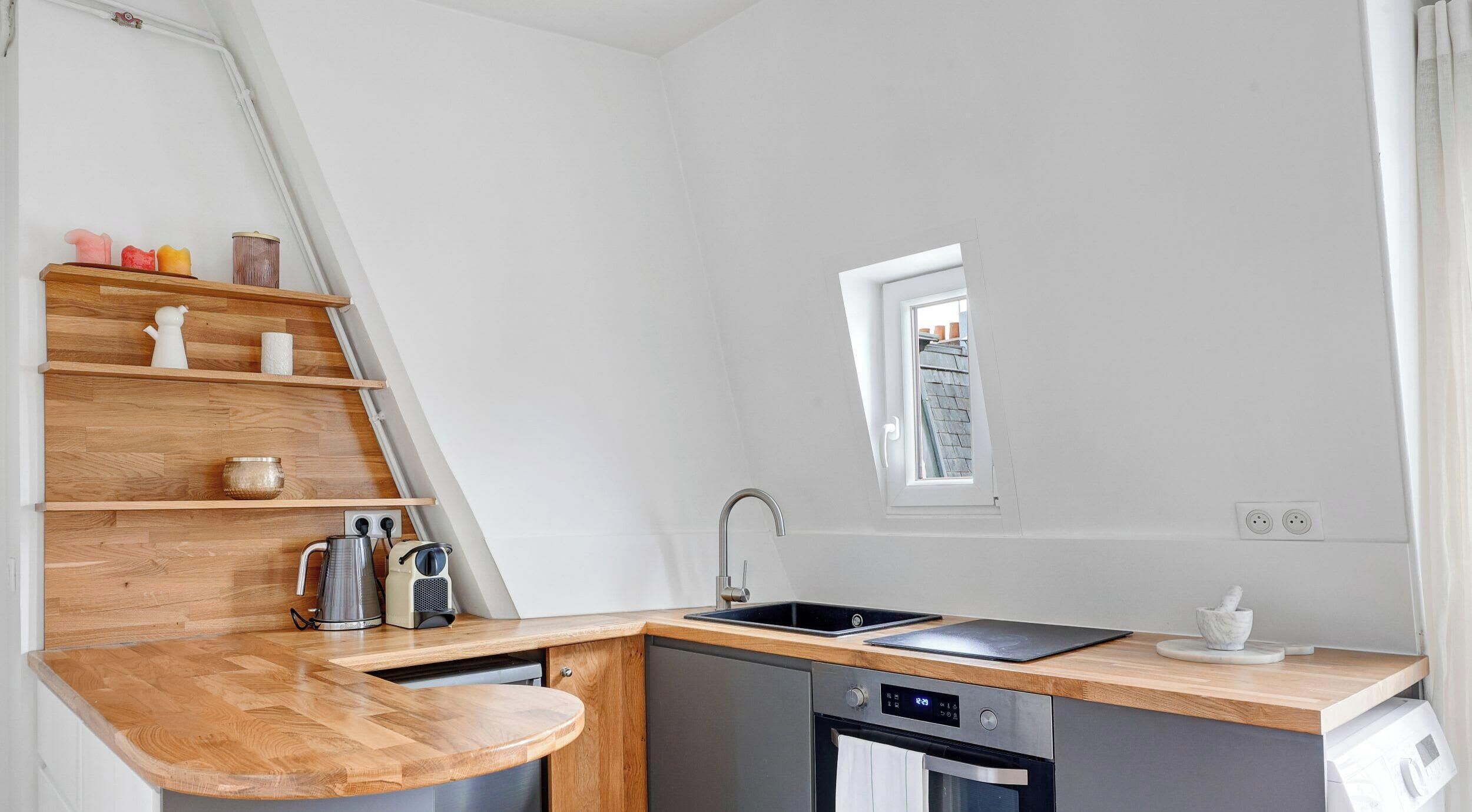 A compact kitchen with a wooden countertop, a built-in dishwasher, a stove, and a window with a view of the outside.