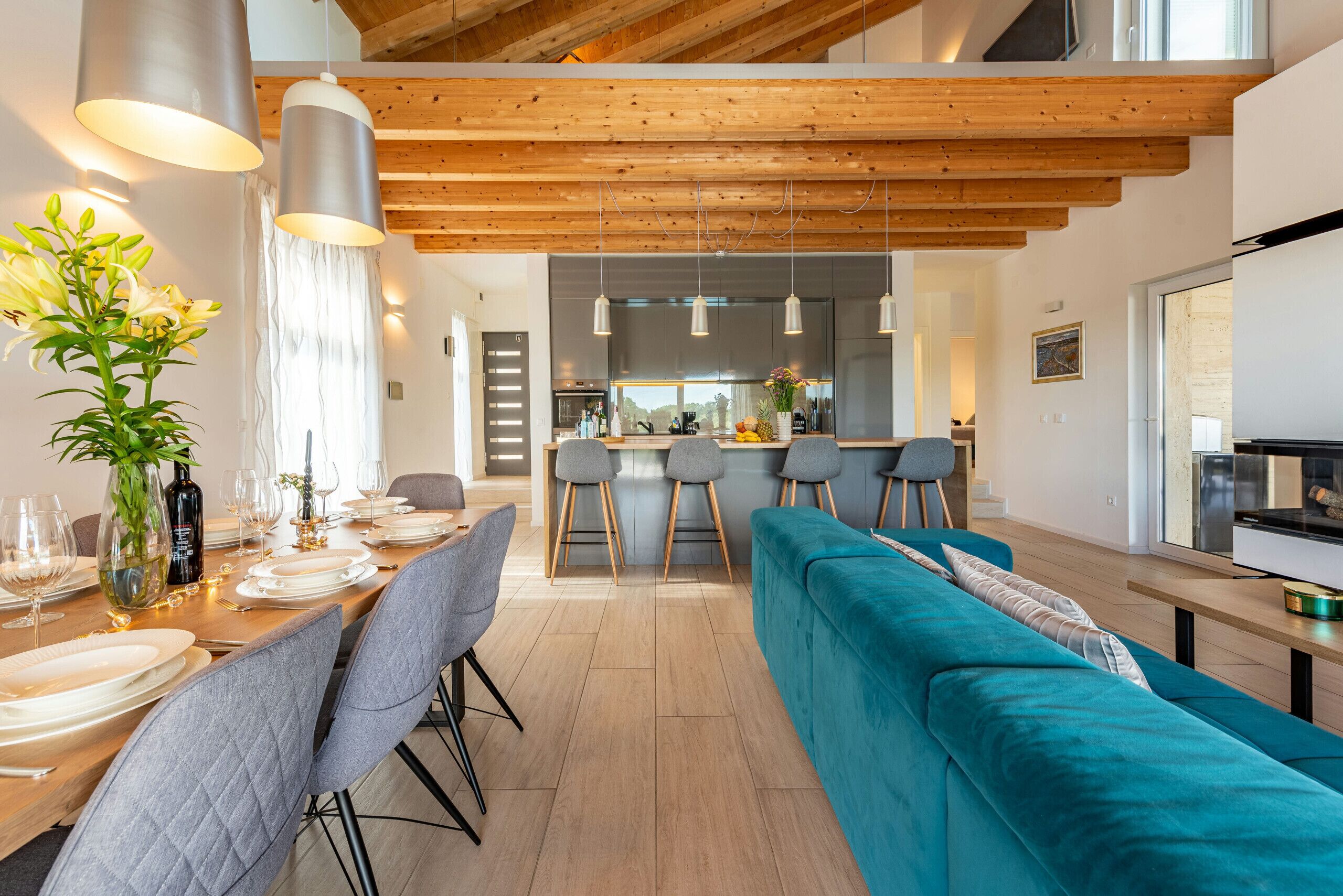 Una cocina moderna con una isla central, iluminación colgante y un sofá color turquesa en un comedor luminoso.